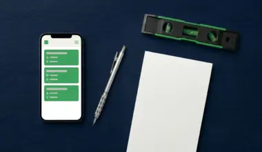 A flat-lay overhead shot of a dark navy workbench with a smartphone displaying a job scheduling app, a mechanical pencil, a closed notepad, and a spirit level, representing job management tools for UK tradespeople.